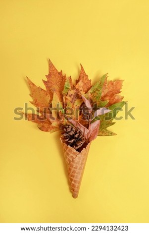 Ice cream cone filled with autumn maple leaves on yellow background