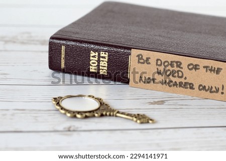 Be doer of the Word, not hearer only, handwritten verse with closed holy bible book and antique golden mirror on wood. A closeup. James 1:22 Scripture, obedience to God Jesus Christ, Christian concept Royalty-Free Stock Photo #2294141971