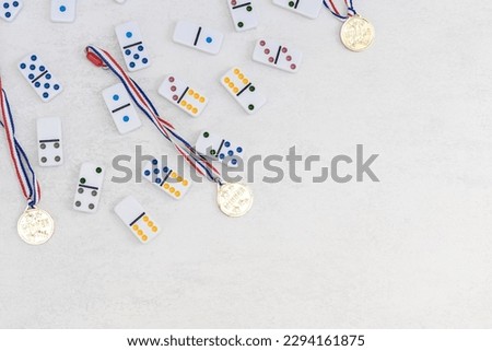 White dominoes with colorful dots and three winner medals lie on the left on a white cement background with copy space on the right,flat lay close-up.Summer board game concept.