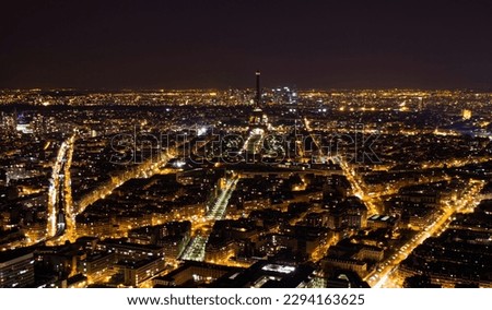 Aerial view of Paris at night with a dark Eiffel Tower and La Défense business district in the background, as seen from the Tour Montparnasse, France