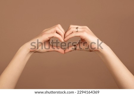 Heart shape from female hands on a beige background