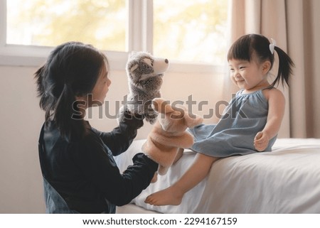 Elder asian sister and younger Asian sister playing animal hand puppet doll toys, sitting on bed, Educational preschool games, Having fun with kid at home concept.; Royalty-Free Stock Photo #2294167159