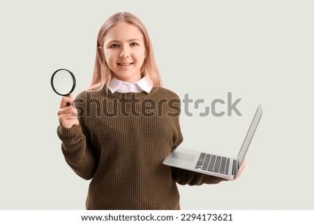 Little girl with magnifier and laptop on green background