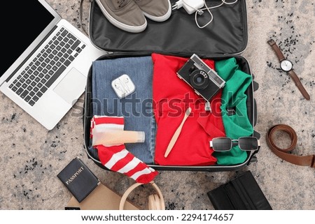 Suitcase with male clothes, laptop and travelling accessories on color carpet