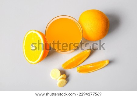 Glass of vitamin C effervescent tablet dissolved in water and oranges on grey background
