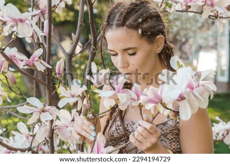 Magnolia flowers, a girl smells a blooming magnolia in the park in the sun, enjoys her vacation.