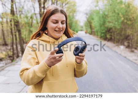 Close up portrait of a lovely happy young girl listening to music through wireless earphones on nature background. Music lover enjoying music. Lifestyle concept.