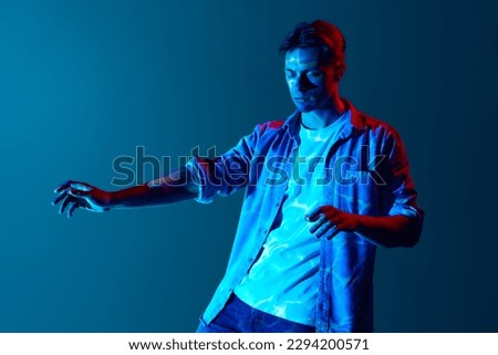 Inner sense, intuition. Young man in casual clothes with closed eyes standing with digital neon filter light reflection over blue background. Concept of modern photography, art, cyberpunk, creativity