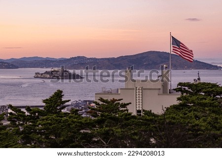 A picture of the American Flag and the Alcatraz Island at sunset.