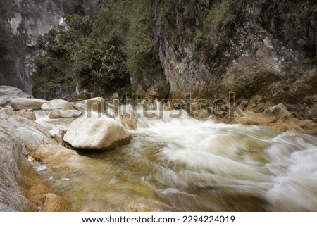 LONG EXPOSURE PHOTO OF WATER RUNNING DOWN A RIVER WITH STONES. CONCEPT OF NATURE AND RIVERS.