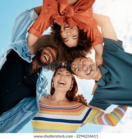 Cheerful group of diverse friends standing in a huddle against a blue sky. Multi-racial millennial friends standing together arms around each other and smiling while looking down at the camera Royalty-Free Stock Photo #2294224611