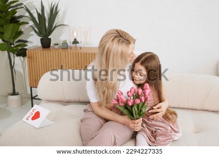 Happy Mother's Day! The child's daughter congratulates her mother and gives her flowers tulips and a card. Mom and girl smile and hug. Family vacation and togetherness.