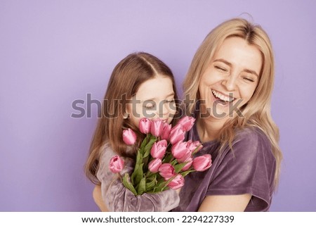 a little girl with her mother and a bouquet of flowers are hugging on a purple background, family holiday and togetherness.