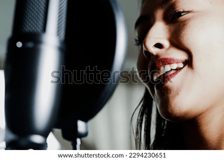 Photograph of a woman singer in a recording studio with dramatic lighting in the background. Concept of people, music and arts.