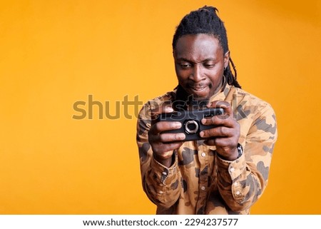 Gamer having fun playing video games on mobile phone, trying to win online gaming competiton. African american man enjoying smartphone videogames in studio over yellow background
