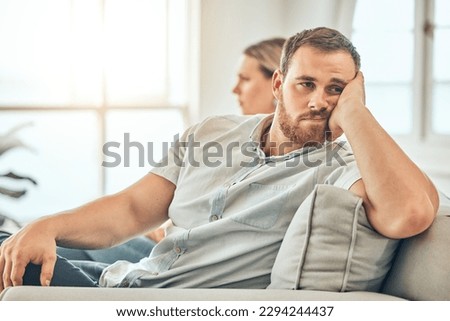 Young caucasian man with a beard looking unhappy and annoyed while sitting on the couch during an argument with his wife at home. Bored man sitting and thinking on the couch. Royalty-Free Stock Photo #2294244437