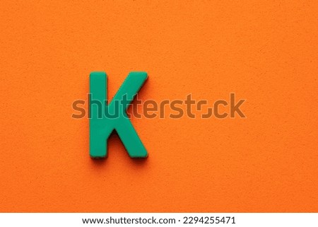 Letter K green plastic uppercase on orange foamy background