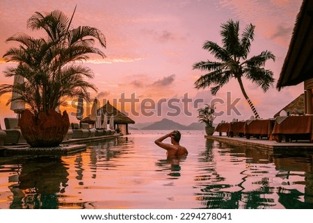 young men in a swimming pool during sunset, Luxury swimming pool in a tropical resort, relaxing holidays in Seychelles islands. La Digue, a Young guy during sunset by swim pool Royalty-Free Stock Photo #2294278041