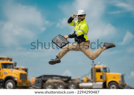 Hispanic builder excited jump and run on site construction. Excited builder construction worker in a safety helmet jumping in front of the trucks. Excited crazy builder man in helmet jump outdoor. Royalty-Free Stock Photo #2294290487