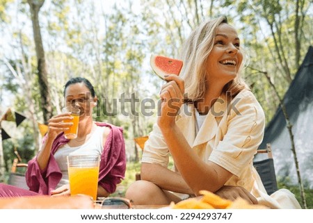 Four international friends having a party during summer in the nature spot, drinking juice and eating melons