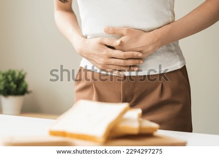 Gluten allergy, asian young woman hand holding, refusing to eat white bread slice on plate in breakfast food meal at home, girl having a stomach ache. Gluten intolerant and Gluten free diet concept. Royalty-Free Stock Photo #2294297275