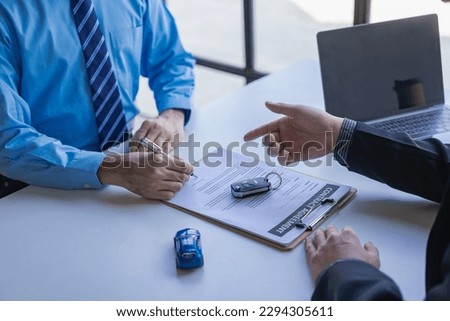 The dealer offers the renter a car introduction purchase contract with keys to sign a signature on the new owner document.