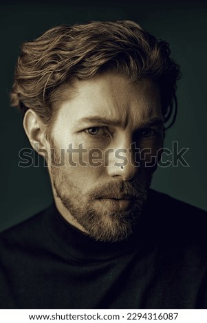 Art portrait in a dark key of a handsome forty-year-old man with curly hair, dressed in a black pullover and a jacket, who looks thoughtfully at the camera. People, emotions. Psychological picture.