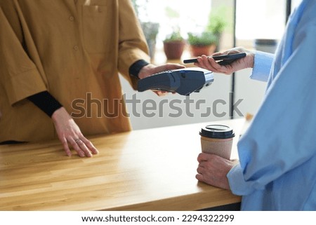Hands of female consumer holding mobile phone over terminal held by young clerk during contactless payment for ordered coffee Royalty-Free Stock Photo #2294322299
