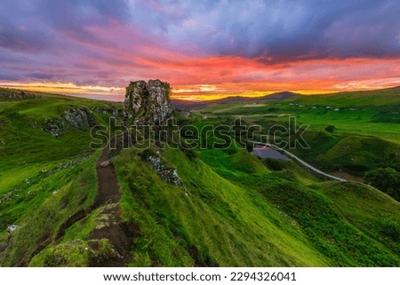 Landscape of an evening mood with sunset in Scotland. Isle of Skye in Scotland in summer. Hiking trail to the rock Castle Ewen with green meadows and hills. Road with a small lake
