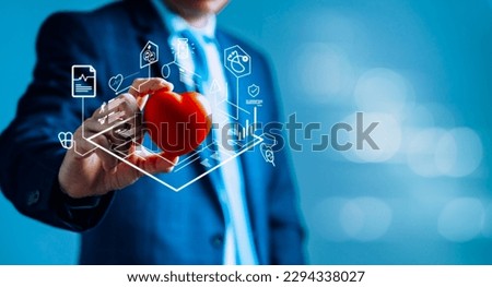 Businessman holding a red heart with medical icons to represent various aspects of modern healthcare, such as digital communication, medical logistics, and healthcare technology