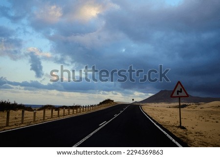 Driving car on black asphalt road through white sandy dunes near Corallejo beach at colorful sunset Fuerteventura, Canary islands, Spain