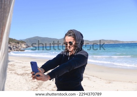 Smiling young girl taking a selfie with smart phone at the beach on sunny day. Happy memories during spring vacation by the seaside.