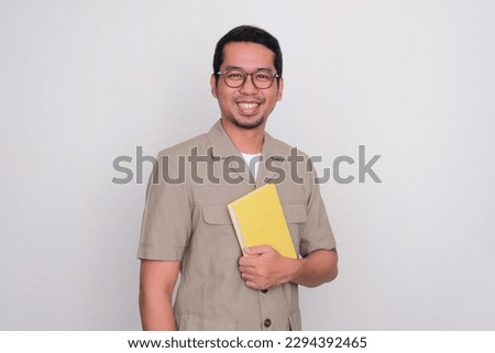 Indonesian school teacher standing proud while holding a book in his chest Royalty-Free Stock Photo #2294392465