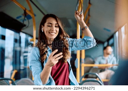 Happy woman text messaging on mobile phone while riding in a bus.  Royalty-Free Stock Photo #2294396271