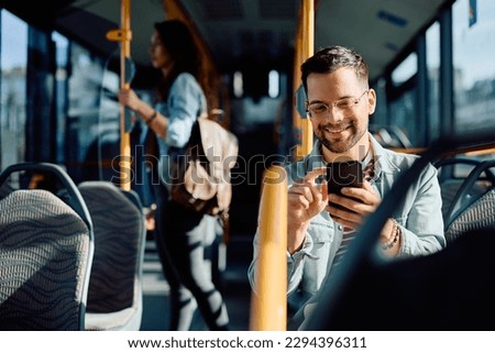 Young happy man using mobile phone while riding in city bus.  Royalty-Free Stock Photo #2294396311