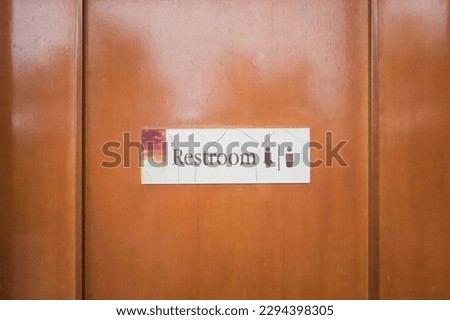 Brown door in a public toilet with a sign Restroom and human icon.