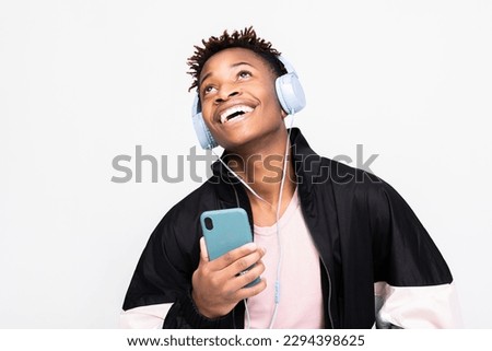 Handsome africam american guy in stylish casual clothes outfit standing over white background n studio isolated smiling holding cell phone like microphone in hands singing wearing wireless headphones.