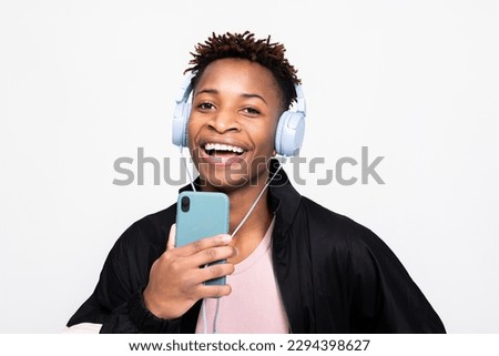 Attractive cheerful american man in casual stylish outfit clothes smiling wearing wireless purple headphones holding cell phone smartphone near mouth singing in phone like microphone.