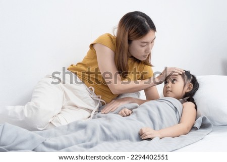 Asian mother measure her sick little daughter body temperature with her hand. Royalty-Free Stock Photo #2294402551
