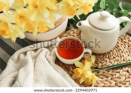 Cup of tea, candles, basket with daffodils, spring aesthetic photo.