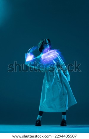 Portrait of fantasy girl with flying hair in stylish coat touching hair with neon reflection of space glow on body on turquoise background. Concept of digital art, fashion, cyberpunk, futurism