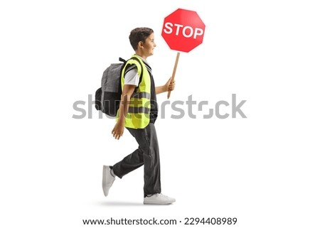Full length profile shot of a schoolboy wearing a reflective safety vest and carrying a stop sign isolated on white background