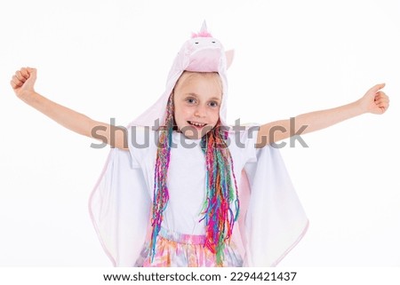 Adorable pretty kid in good mood looking at camera smiling showing thumbs up looking into distance posing while shooting process standing on white background in studio isolated.