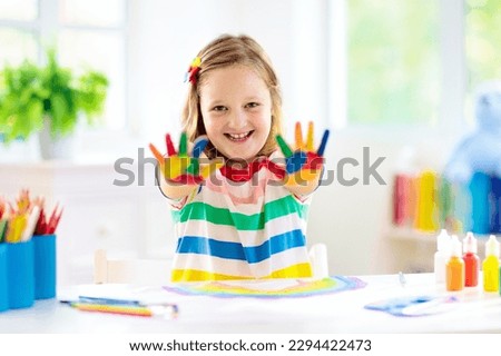 Kids paint. Child painting in white sunny study room. Little girl drawing rainbow. School kid doing art homework. Arts and crafts for kids. Paint on children hands. Creative little artist at work.