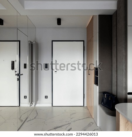 Minimalist composition of vestibule with white door, marble tiles, mirror on the wall, lamela door, gray radiator and personala accessories. Home decor. Template. 
