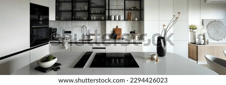 Modern composition of kitchen space with design kitchen island, grey table, black vase with flowers, furnitures and elegant personal accessories. Stylish home decor. Template. 
