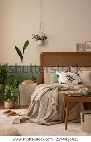 Warm and cozy bedroom interior with mock up poster frame, boho bed, beige bedding, green wall with stucco, books, brown slippers, plants in pots and personal accessories. Home decor. Template. Royalty-Free Stock Photo #2294426423