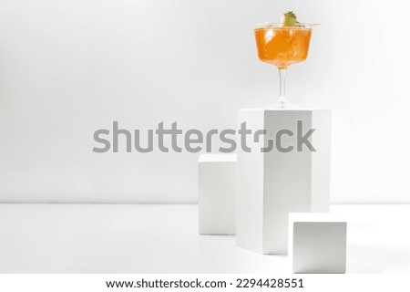 Aperol Spritz cocktail with ice cubes and a slice of cucumber in a transparent stemmed glass. The cocktail stands on a plaster figure among other plaster figures on a white background.
