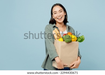 Young cheerful happy woman wear casual clothes hold brown paper bag with food products after shopping isolated on plain blue cyan background studio portrait. Delivery service from shop or restaurant