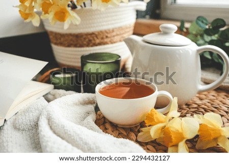 Cup of tea, candles, open book, basket with daffodils, spring aesthetic photo.